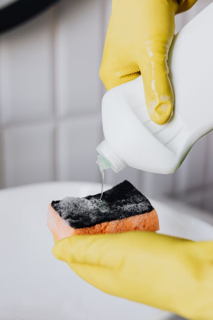 Crop faceless person in yellow latex protective gloves pouring cleaning agent from bottle to sponge in bathroom