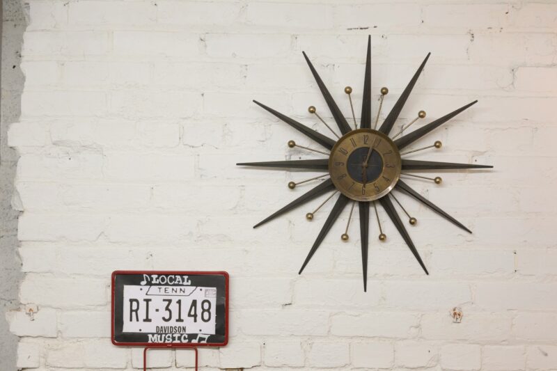 Brown and black sun designed analog wall clock at 6:05