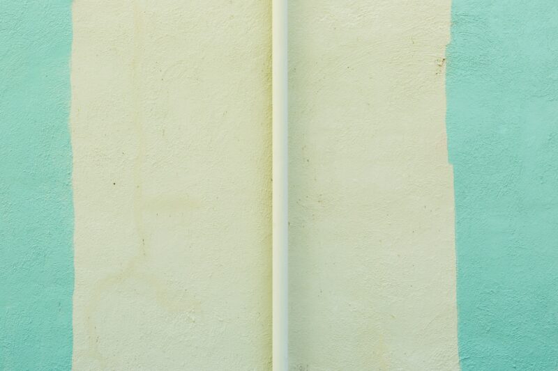 A white surfboard leaning against a blue and green wall