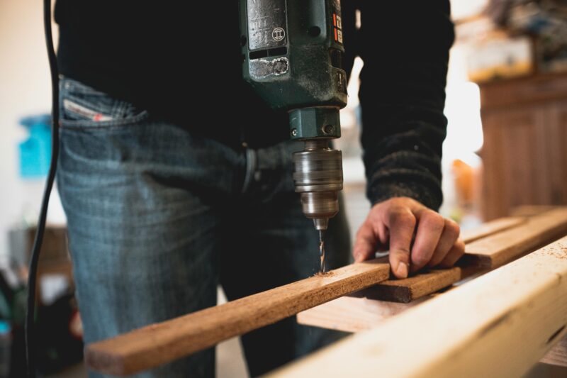 Close-up of a person using an electric drill on a wooden plank, showcasing detailed woodworking skills.