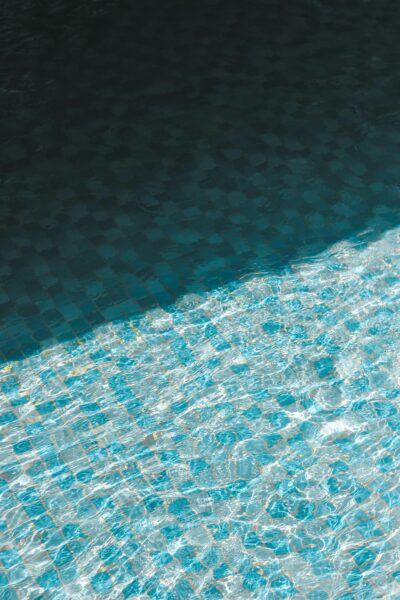 A tranquil view of a swimming pool with blue tiles and shimmering water reflecting sunlight.