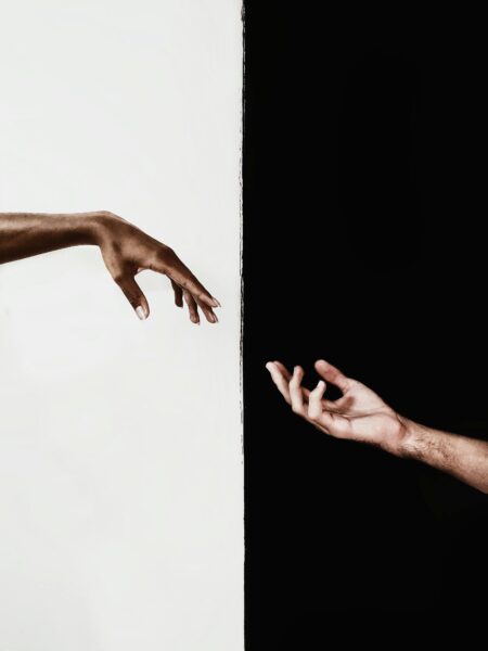 Two hands reaching across a stark black and white divide, symbolizing connection and unity.