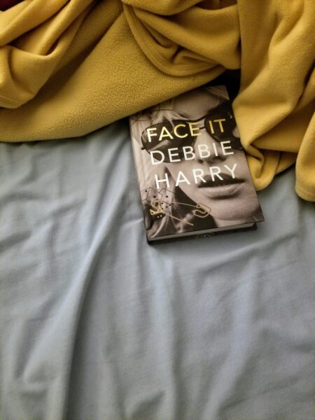 A cozy setup showing the book 'Face It' by Debbie Harry on a bed with soft sheets.