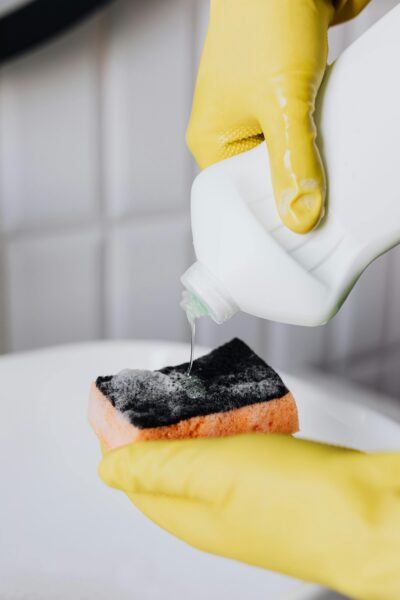 Crop faceless person in yellow latex protective gloves pouring cleaning agent from bottle to sponge in bathroom