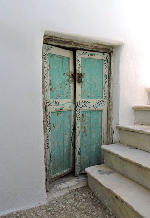 Charming rustic doorway with turquoise wooden panels beside aged concrete stairs.