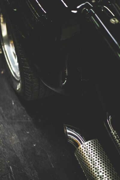 Detailed view of a vintage car's shiny chrome exhaust and tire reflecting ambient light.