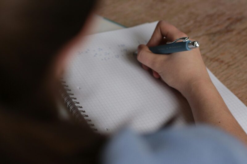 A student writes mathematical notes in a notebook using a pen, focus on studying.