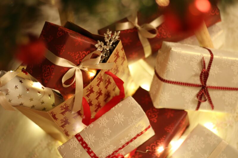 Beautifully wrapped Christmas presents under the tree with festive decorations and ribbons.