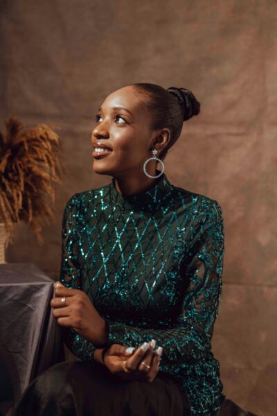 Elegant indoor portrait of African woman in a green sequin dress, smiling softly.