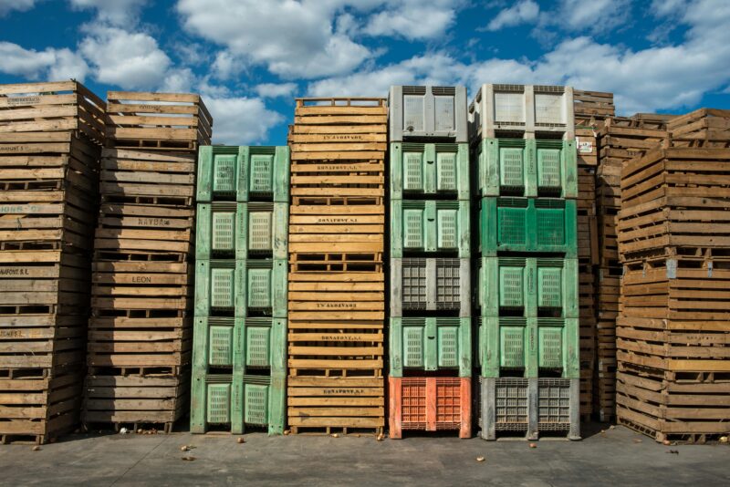 Stacks of wooden and plastic pallets under a blue sky, perfect for logistics and distribution themes.