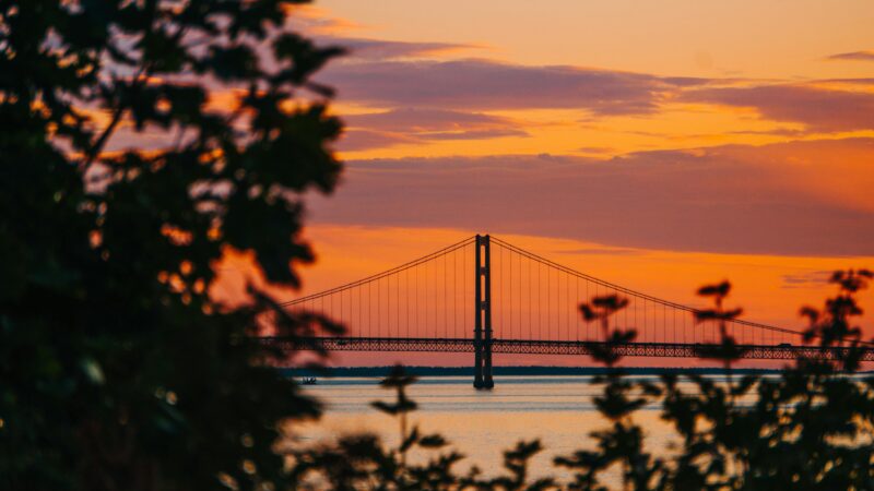 A stunning view of Mackinac Bridge at sunset with an orange sky and silhouette foreground.