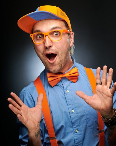 Expressive man in colorful cosplay attire with orange accessories, surprised expression.