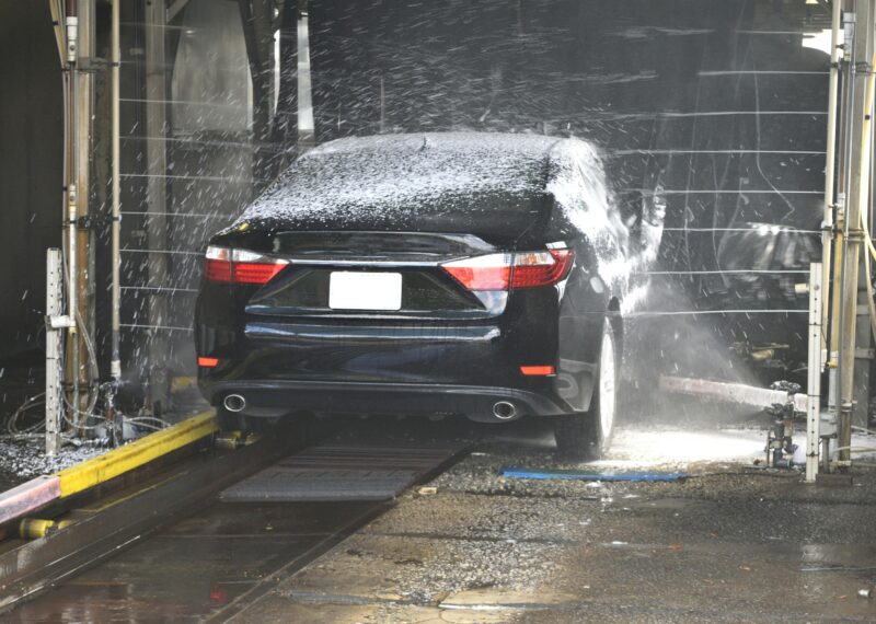 A black car being cleaned in an automated car wash with water and foam.