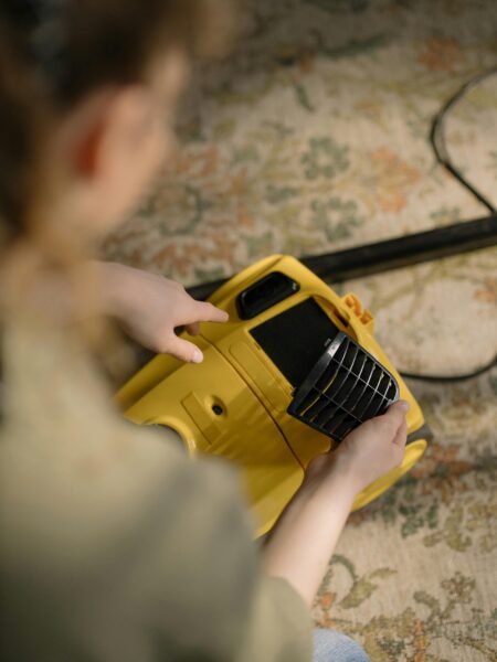 A person cleans and maintains a yellow vacuum cleaner on a patterned carpet indoors.