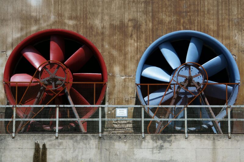 Close-up of large red and blue industrial fans on a rustic wall showcasing machinery and ventilation.