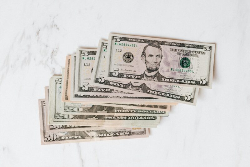 Stack of various US dollar bills on a clean marble surface, emphasizing finance and currency.