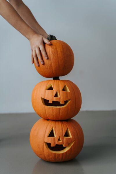 Three carved Jack-o'-lanterns stacked on top of each other with a hand adjusting the top pumpkin.