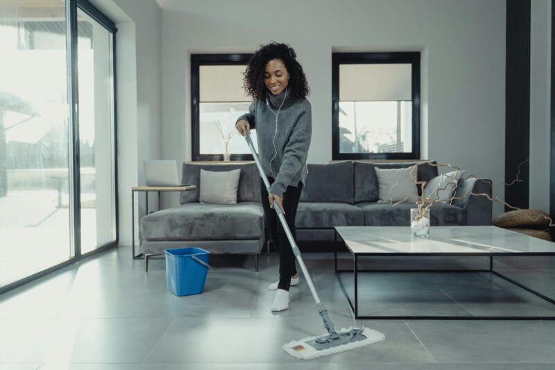 Woman mopping living room floor while listening to music in a cozy home setting.