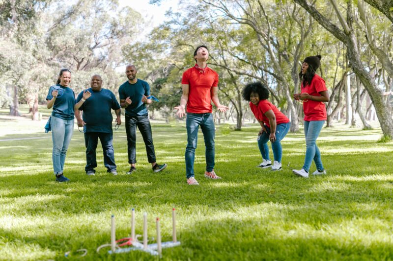 A multiracial group of adults enjoying a fun game of ring toss outdoors in a sunny park setting.