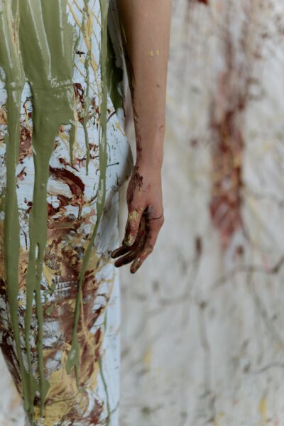 Close-up of a hand covered in paint against a splattered wall, embodying artistic chaos.