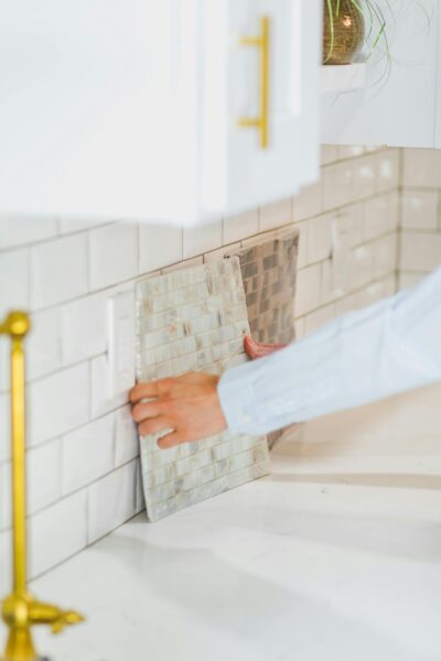 Person installing tile backsplash in a bright, modern kitchen setting.