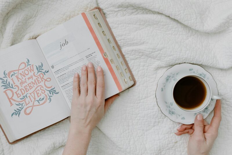 Top view of morning Bible study with coffee, featuring open Bible and feminine hands.