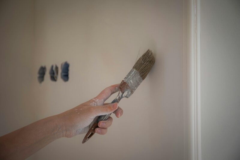 Close-up image of a hand painting a wall with a brush for home renovation.