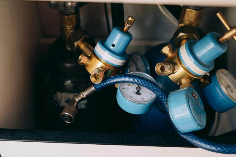 Detailed view of blue and brass gas pressure regulators with gauges and tubing in an industrial setting.