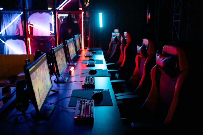 High-tech gaming setup with PCs, RGB lighting, and gaming chairs in a gaming house.