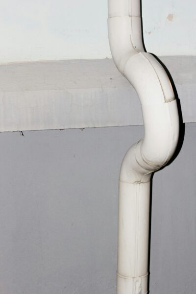 Vertical shot of a curved white drainage pipe against a concrete wall.