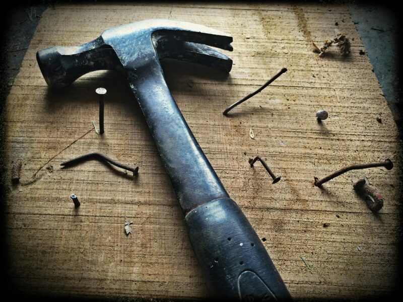 A weathered hammer surrounded by bent nails on a wooden plank, carpentry work