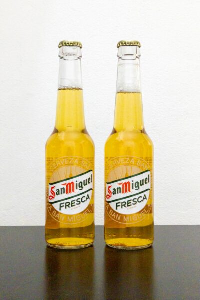 Two San Miguel Fresca beer bottles on a table with a white background.