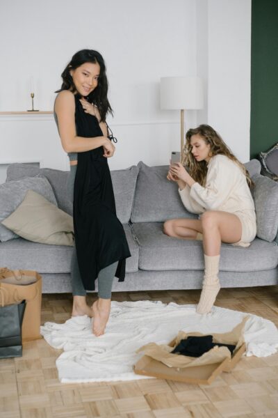 Two women relaxing while trying on new clothing purchases in a cozy living room setting.