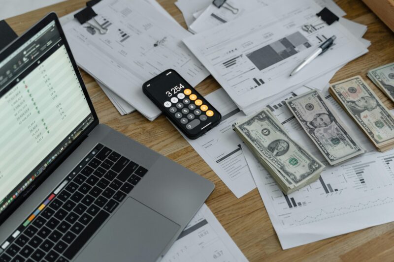 Financial documents and currency with laptop and phone calculator on desk for net worth analysis