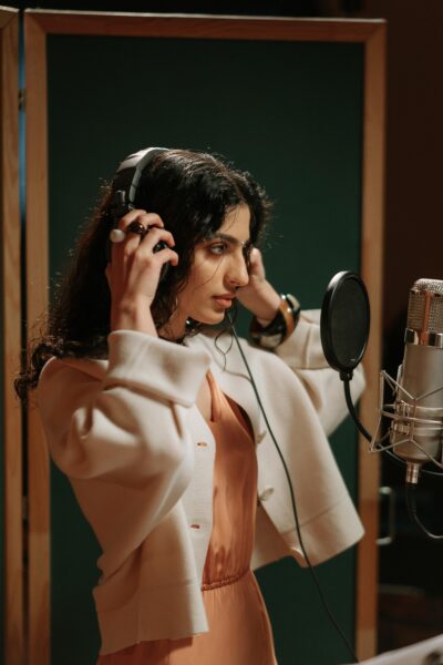 Female vocalist adjusting headphones while recording music in a studio.