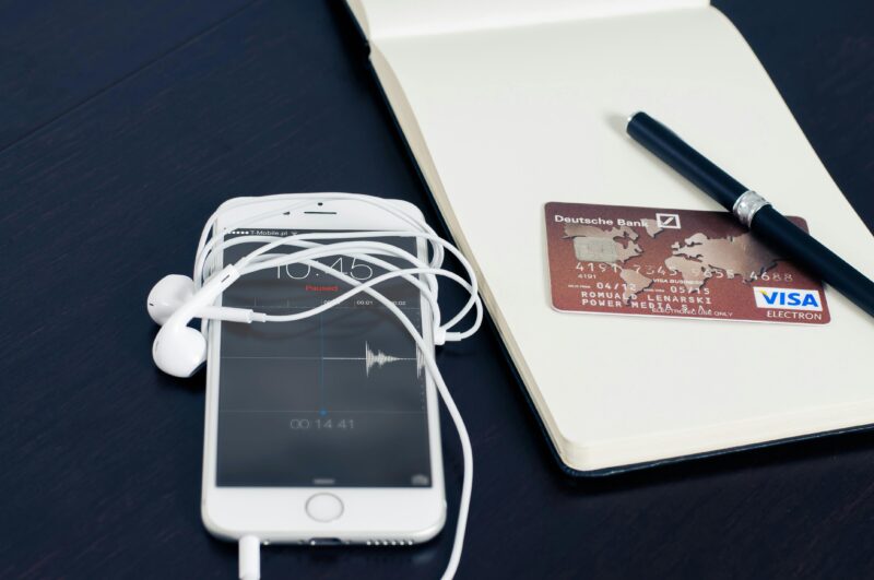 A white smartphone with earbuds, credit card, and pen on a notepad, symbolizing tech and finance.