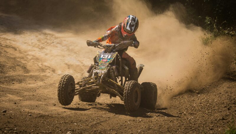 Thrilling action shot of a racer maneuvering an ATV on a dusty dirt track during daytime.