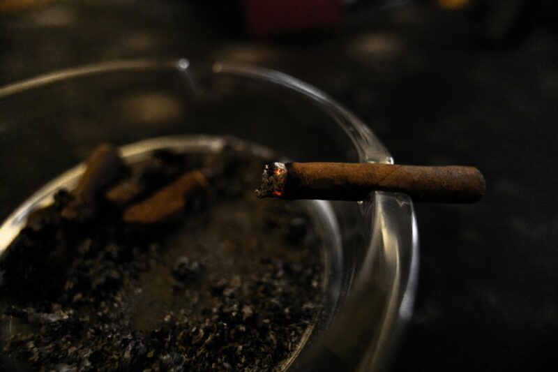 Detailed shot of a cigarette burning in a glass ashtray, symbolizing smoking habit.