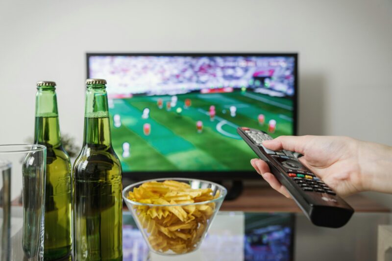 A person watching soccer on TV with snacks on the table.