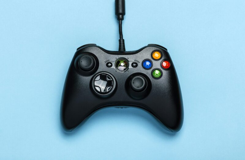 Black video game controller isolated on a blue background for gaming enthusiasts.