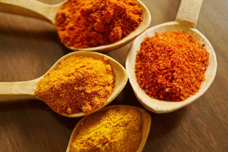 Close-up of vibrant spices like turmeric and chili powder in wooden spoons.