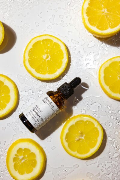 Lemon slices and Vitamin C serum bottle on wet surface, bright skincare concept.