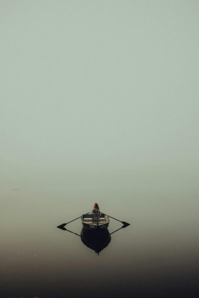 A peaceful scene of a lone person rowing a boat in a misty, fog-covered lake.