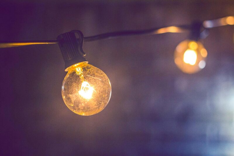 Close-up of an illuminated vintage-style string light bulb on a dark background.