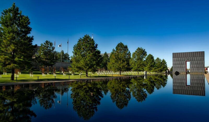 Serene memorial park with a monument and water reflection under clear blue sky.