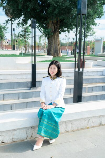 A woman in traditional attire sits on steps in an outdoor urban setting.