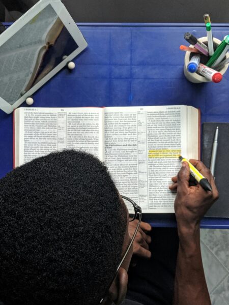 Man highlighting text while studying with a book and tablet on a desk.