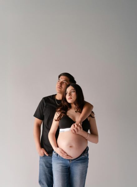 Expecting couple in casual jeans, embracing in a light studio setting, conveying love and anticipation.