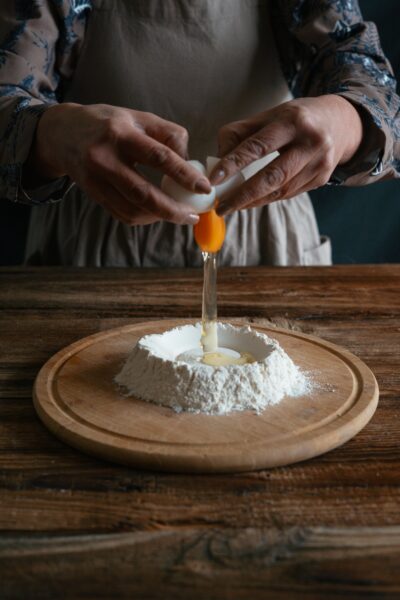 Close-up of hands cracking an egg into a flour well on a wooden board during baking preparation.