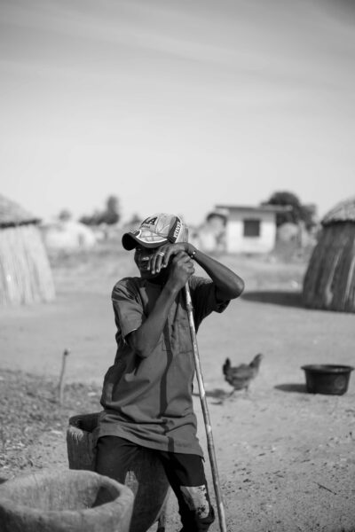 Monochrome image of a young boy in a rural village setting with huts.